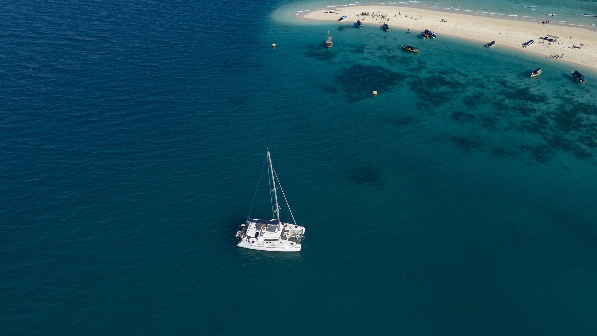 Aerial view of a catamaran anchored by a white sandbank in turquoise water off Zanzibar