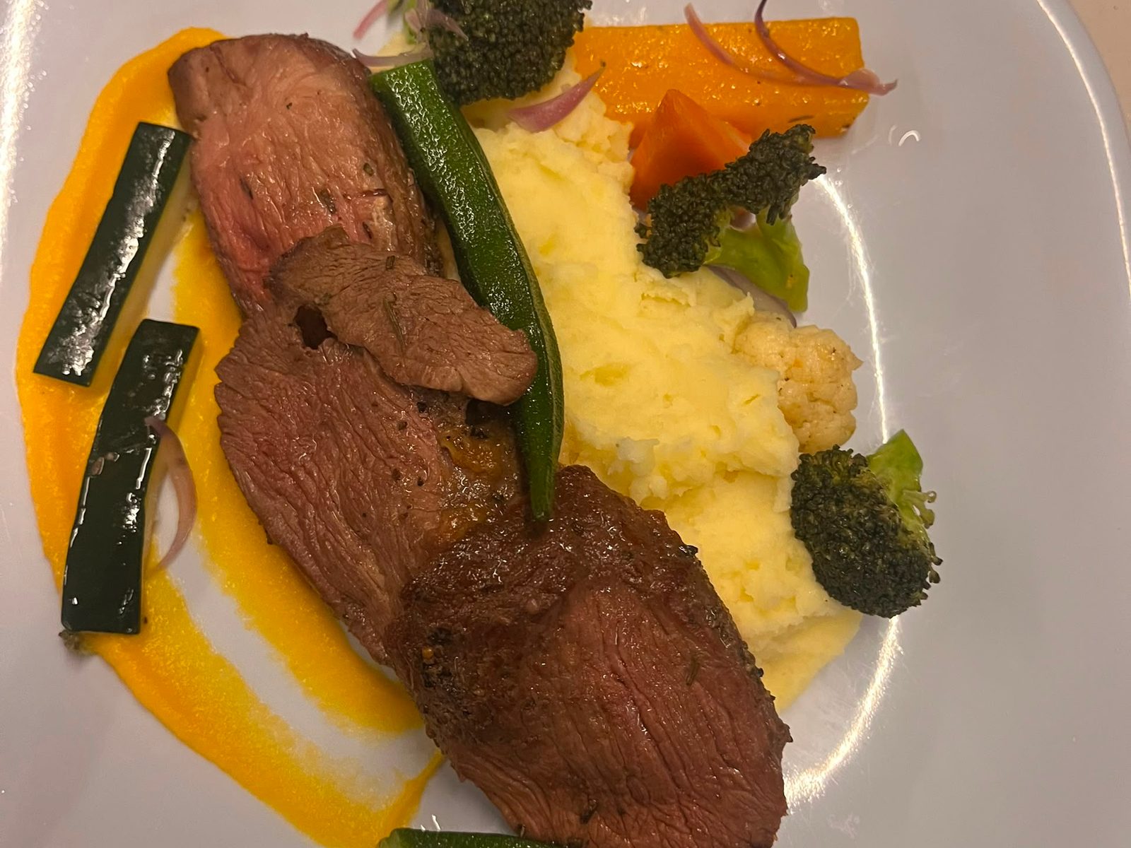 Plated dinner of sliced grilled meat with mashed potato and vegetables on board
